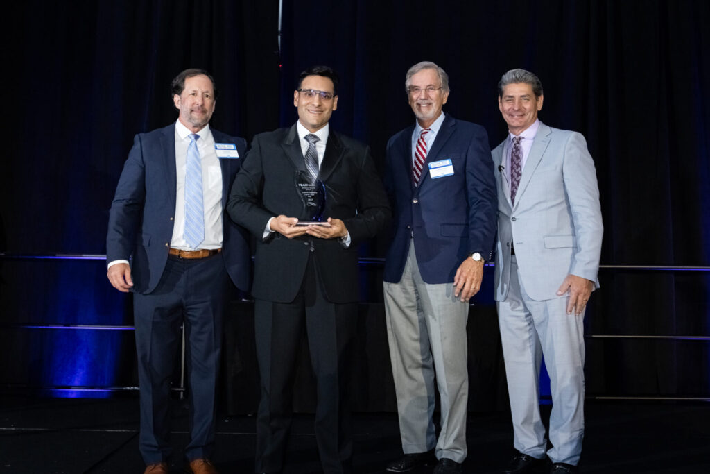 Dr. Gabriel Alejandro Lopez Vega smiles on stage with his award in his hands. Dr. Jody Crane, Dr. Lynn Massingale, and Michael Wiechart pose with him.